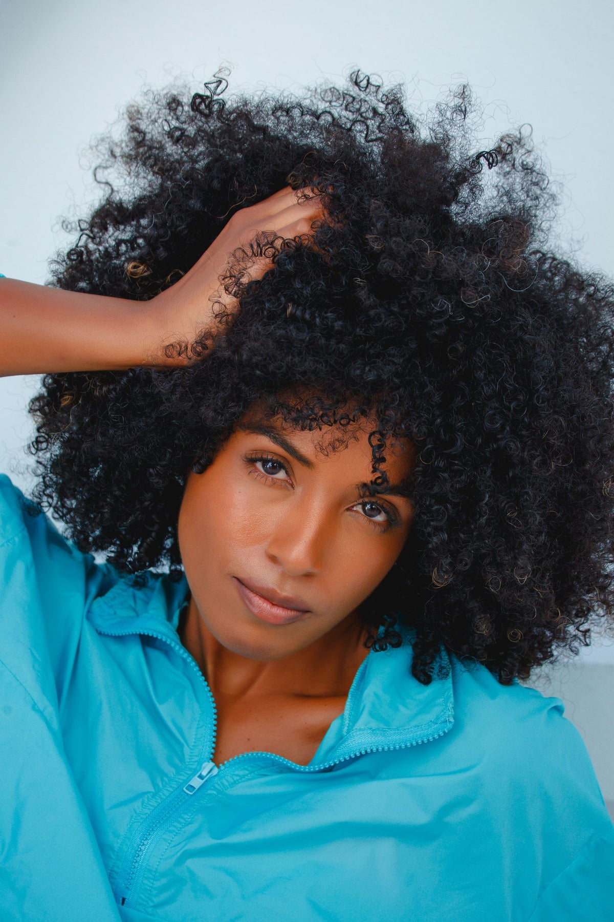 Woman with coily natural hair lifting a section to look at the curl pattern